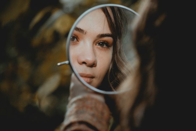 Young woman looking in a mirror: Self-awareness is the beginning of all growth.